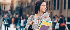 A young woman with books in her hand smiles.